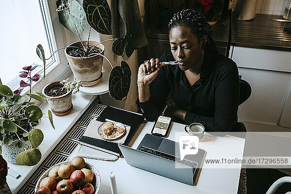 Junge Unternehmerin sitzt mit Laptop bei der Arbeit von zu Hause aus