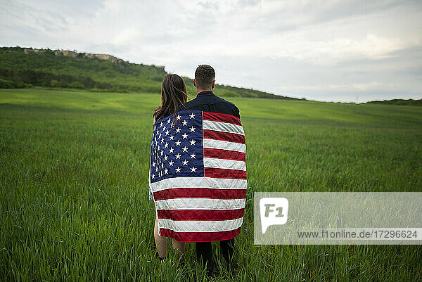 Rückansicht eines jungen Paares in amerikanischer Flagge  das in einem Weizenfeld steht