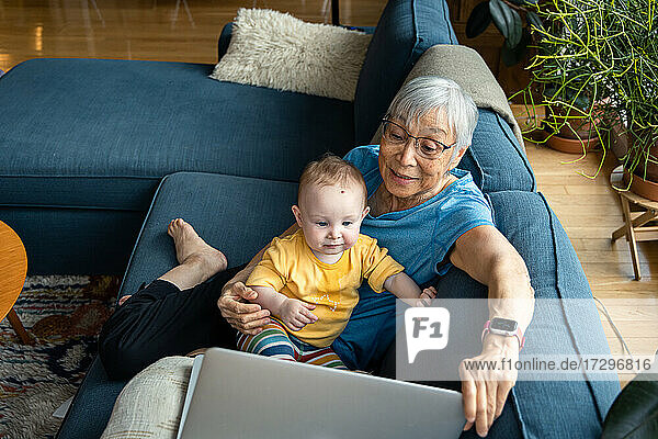 Großelternteil sitzt mit Enkelin und benutzt Laptop für Videoanrufe