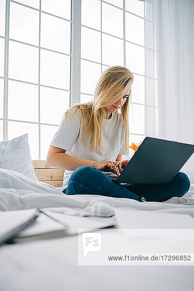 blonde girl working on laptop in bed