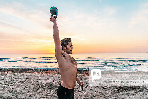 muskulöser Mann beim funktionellen Training mit der Kettlebell am Strand von