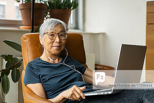 Porträt einer älteren Frau  die Kopfhörer trägt  während sie zu Hause einen Laptop benutzt