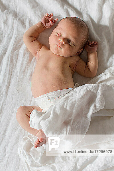 Newborn baby sleeping on white bed with white sheets