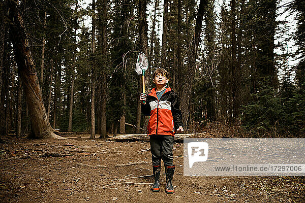 Junge hält Fischernetz im Wald und trägt eine rote Jacke