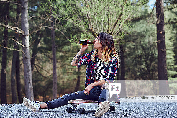 Eine junge Frau sitzt auf einem Skateboard und trinkt Bier.