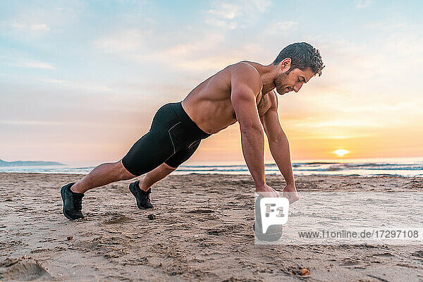 muscular man training core on the beach at sunrise