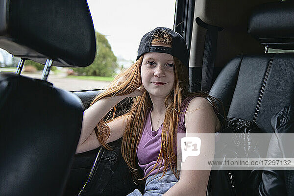 Tween girl with red hair and backwards baseball hat in car.