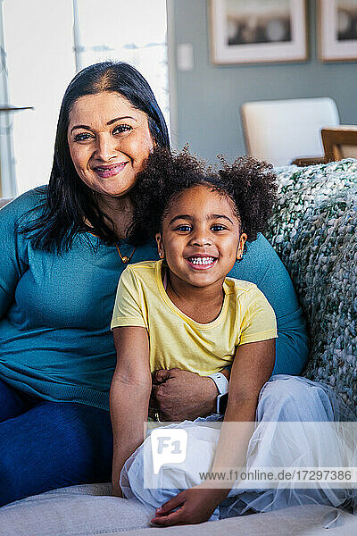 Porträt eines lächelnden niedlichen Mädchens  das mit seiner Großmutter auf dem Sofa zu Hause sitzt