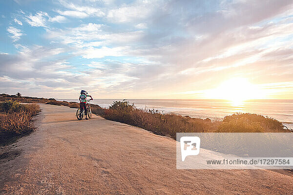 Ein Junge mit einem bunten Hemd fährt mit dem Fahrrad auf einem Küstenweg.