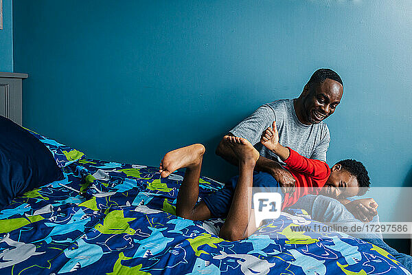 Verspielter Vater und Sohn auf dem Bett bei der gemeinsamen Freizeitgestaltung zu Hause