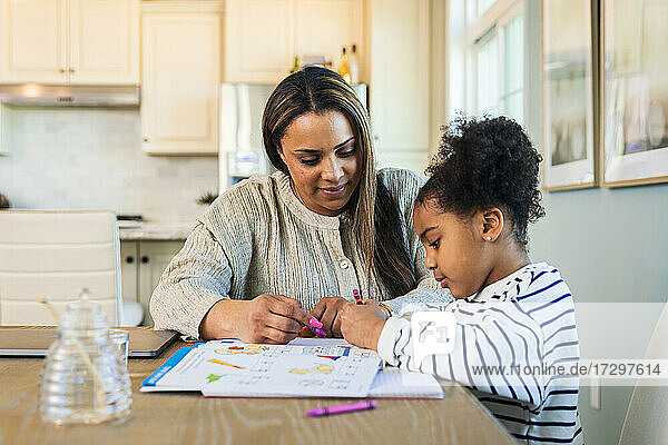 Mother teaching cute mixed race daughter sitting at table