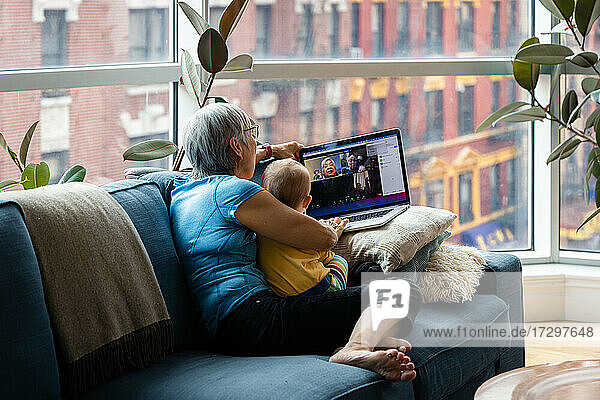 Ältere Frau sitzt mit ihrer Enkelin zusammen und führt einen Videogespräch über einen Laptop im heimischen Wohnzimmer