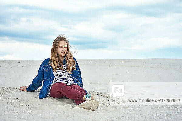 Teenager-Mädchen sitzt auf dem Sand und schaut in die Ferne