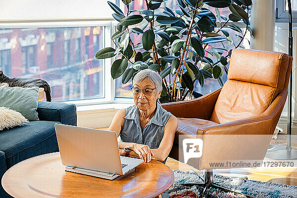 Ältere asiatische Frau sitzt und benutzt einen Laptop zu Hause im Wohnzimmer
