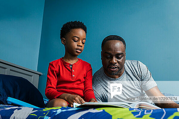 Vater arbeitet mit Sohn an seinen Hausaufgaben zu Hause auf dem Bett