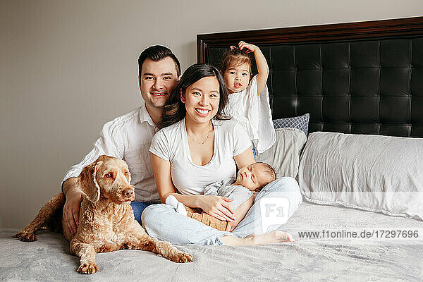 Happy multiracial family with children and dog pet on bed at home