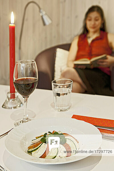 Caprese-Salat auf einem Tisch mit einer lesenden Frau im Hintergrund