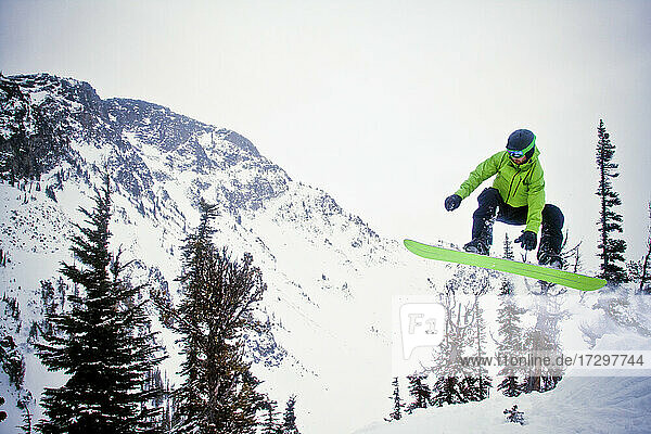 Snowboarder in grüner Kleidung in der Luft nach dem Absprung von einer Schanze.
