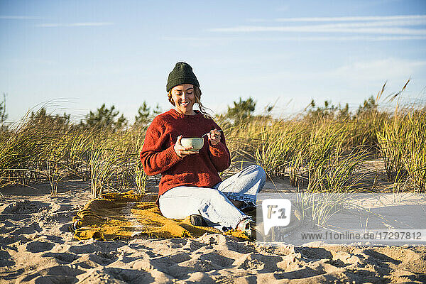Junge Frau  die eine Suppe genießt  während sie allein im Auto am Strand campiert