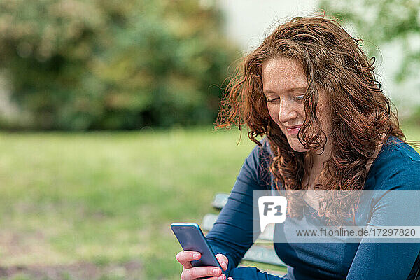 Portrait of charming redhead young woman with smartphone in a park