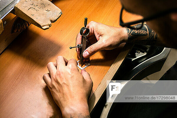 Männerhände in einer Juwelierwerkstatt  die ein Silberstück mit Kompass markieren