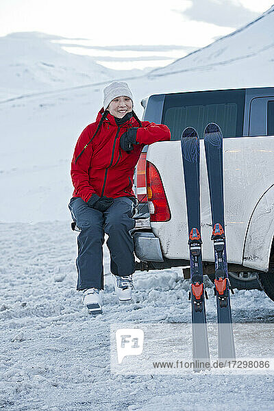 Frau sitzt auf der Rückseite eines Pick-ups und macht eine Pause vom Skifahren