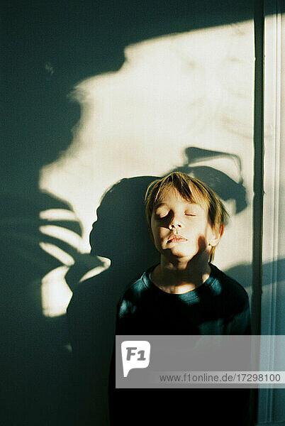 Little boy with shadows across his face and the wall behind him