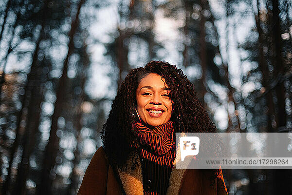 Porträt einer lächelnden jungen Frau  die im Winter inmitten von Bäumen steht