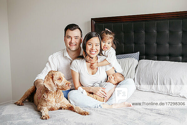 Glückliche multirassische junge Familie mit Kindern und Hund auf dem Bett.