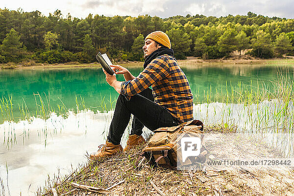 Spanish traveler enjoying reading a book sitting on a peaceful lake