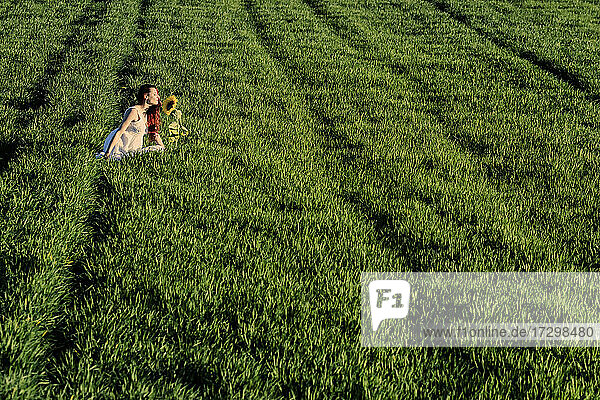 Frau riecht an einer vereinzelten Sonnenblume in einem grasbewachsenen Feld