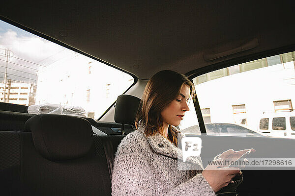 Nicht-binäre Frau benutzt Smartphone während der Fahrt im Auto