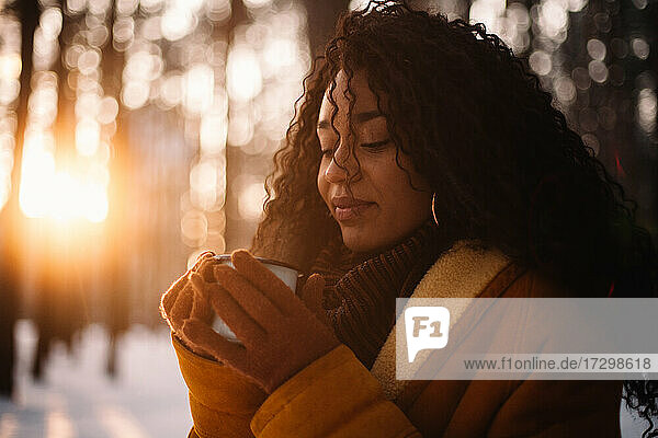 Junge Frau mit einer Tasse Tee in einem Park im Winter bei Sonnenuntergang