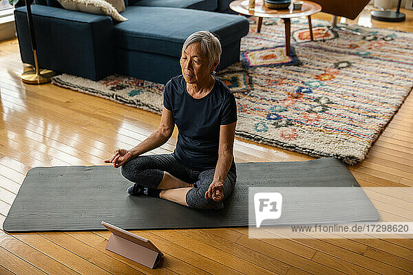 Ältere Frau meditiert  während sie zu Hause über ein digitales Tablet lernt