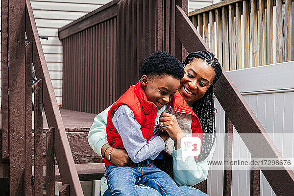 Fröhliche Mutter und Sohn sitzen auf den Stufen im Hinterhof