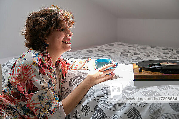 Young hipster girl listening music on a turntable  smiling and drinking coffee