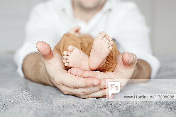 Nahaufnahme eines Vaters  der die Füße eines kleinen Neugeborenen in seinen Händen hält.