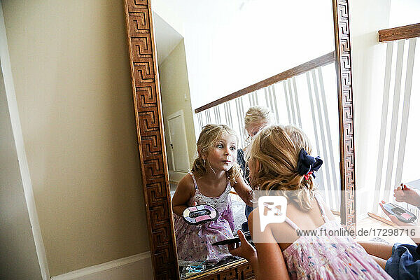 Kleines Mädchen betrachtet sich selbst im Spiegel und trägt Make-up