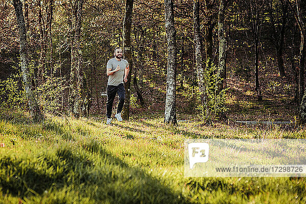 Man in cap and dark tracksuit running through the forest
