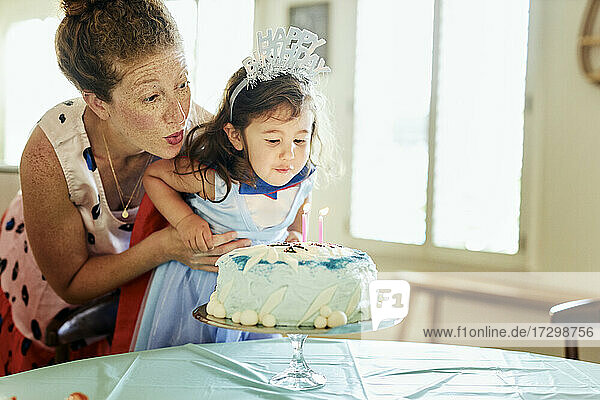 Mutter und Tochter blasen zu Hause Kerzen auf der Geburtstagstorte aus