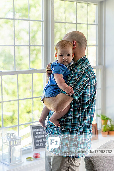 Man holding baby boy near window.