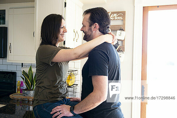 Attraktiver Mann und Frau umarmen sich und lachen in der Küche.
