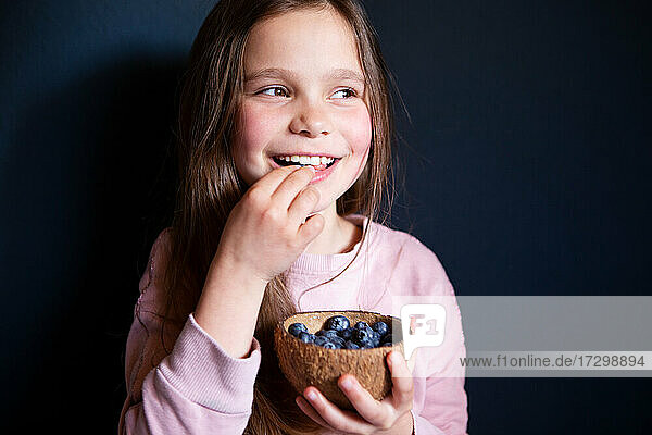 Lächelndes Mädchen pflückt frische Blaubeeren auf dunklem Hintergrund