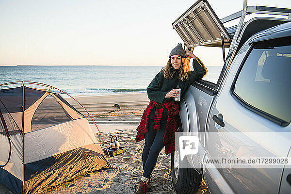 Junge Frau genießt Kaffee im Reisebecher beim Camping am Strand