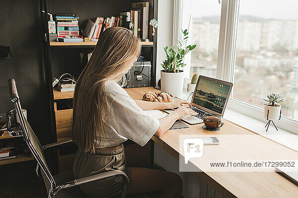schöne Frau  die zu Hause an einem Laptop arbeitet und am Fenster sitzt