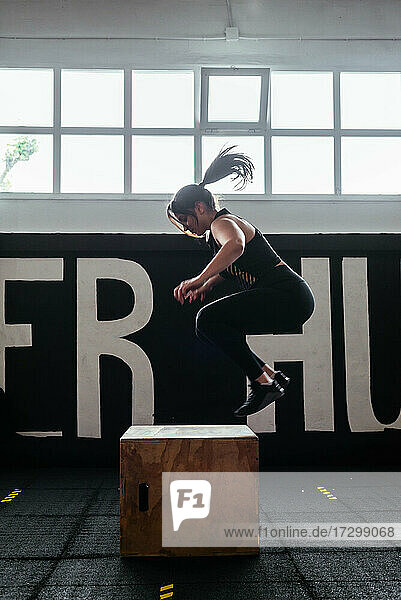 Sportliche Frau springt zum Training auf einen Turnkasten