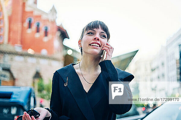 Stylish young girl in black dress talking on the phone on the city street