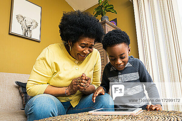 Fröhlicher Junge und Großmutter spielen ein Videospiel auf einem digitalen Tablet bei sich