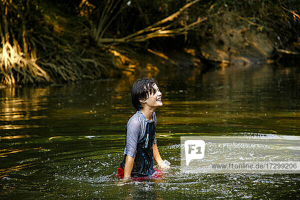 Ein glücklicher Junge spielt in einem Fluss im goldenen Sonnenlicht des Sommers