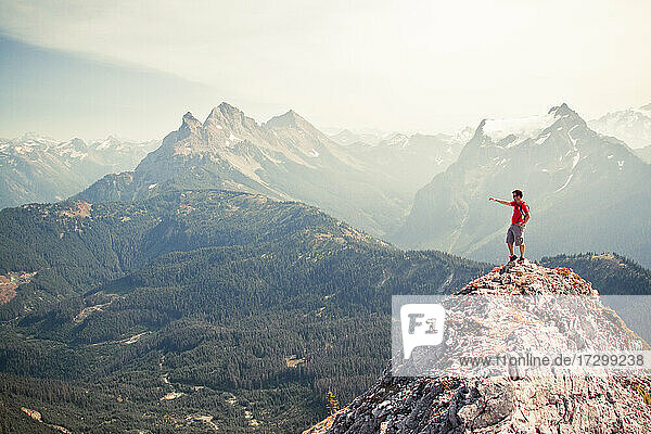 Wanderer  der vom felsigen Berggipfel über das Tal zeigt